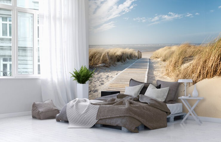 Low bed with grey and white bedsheets in front of a beach themed wallpaper