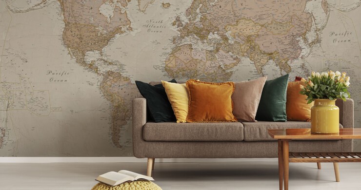 Wallpaper trends for 2023 in a living room with a beige sofa and muted orange and mustard cushions with a beige world map wall mural