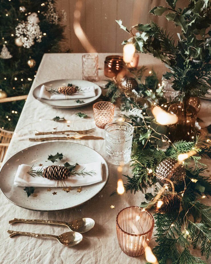 Christmas table with beige table cloth and plates with pinecones and gold cutlery 